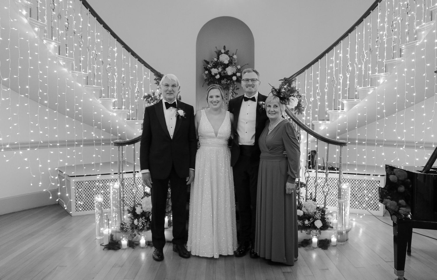 Black and white photo of formal event with elegant decor, wedding party under arch with string lights and candles.