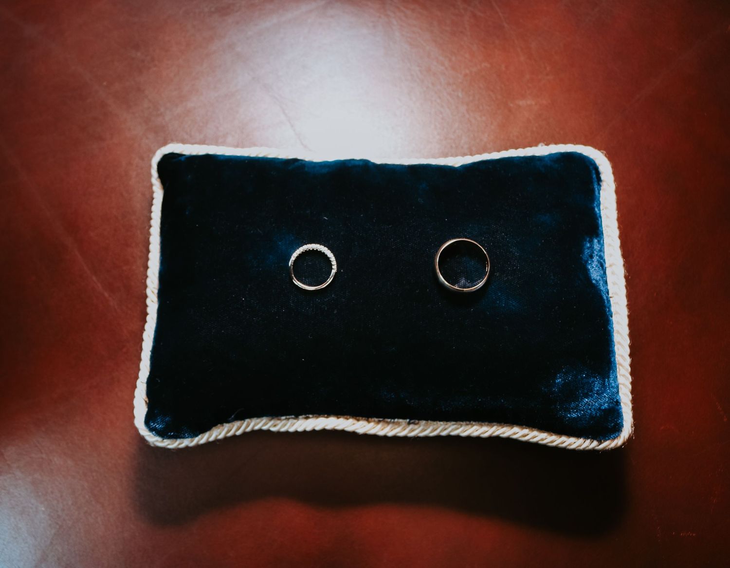 Two wedding rings displayed on a navy blue velvet pillow against a dark red background.