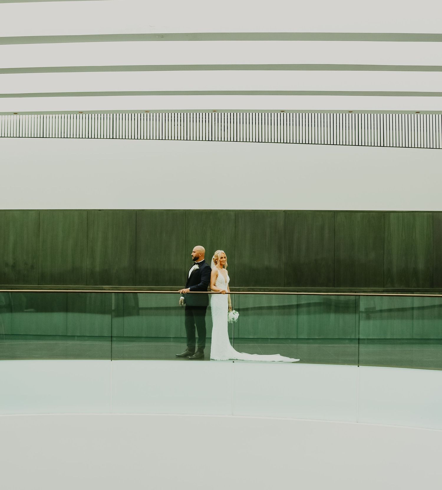 Minimalist wedding portrait with couple reflected in modern architectural setting with green wall.