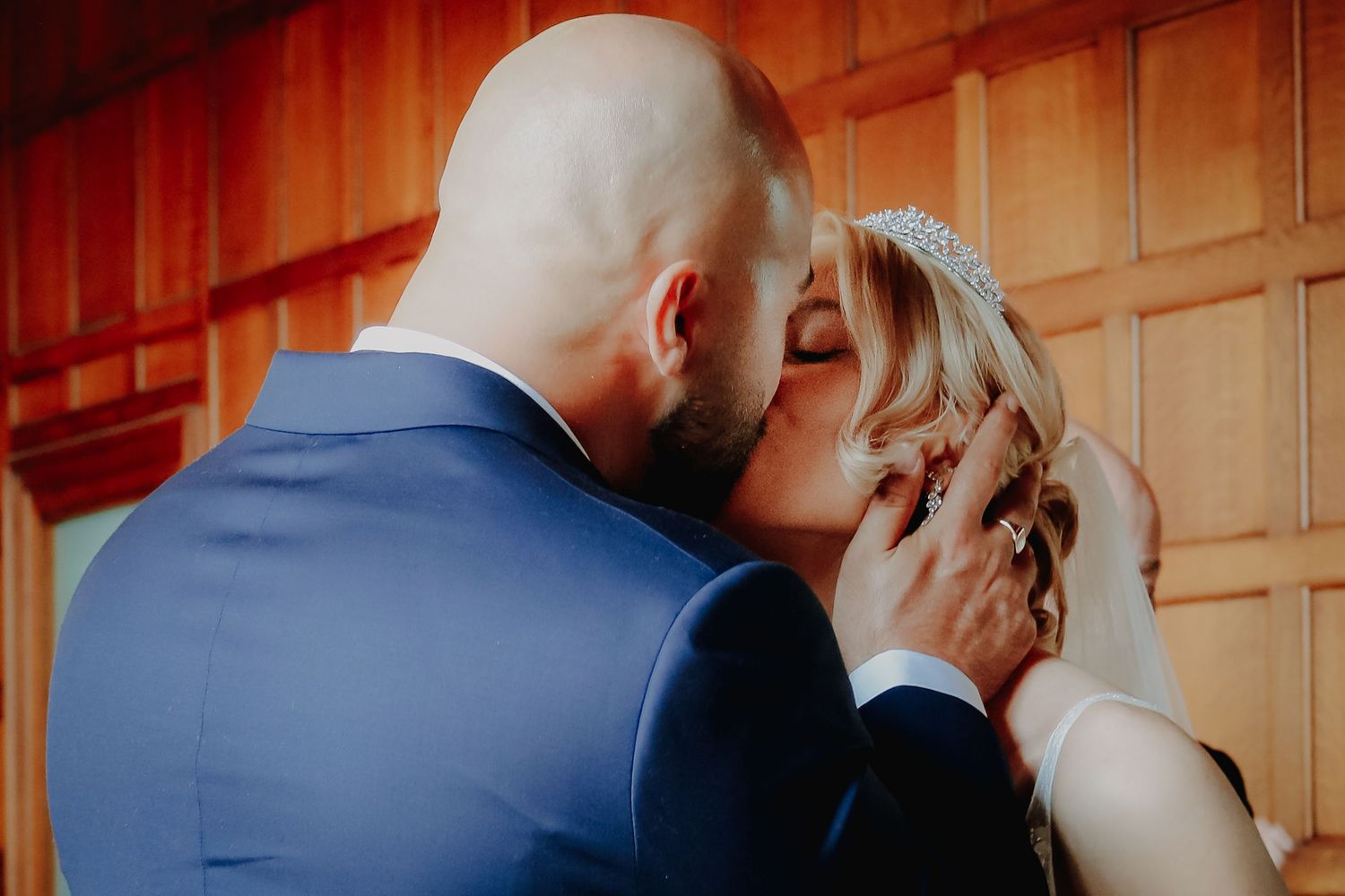 A tender intimate moment shared between couple during their wedding ceremony against wooden paneled backdrop.