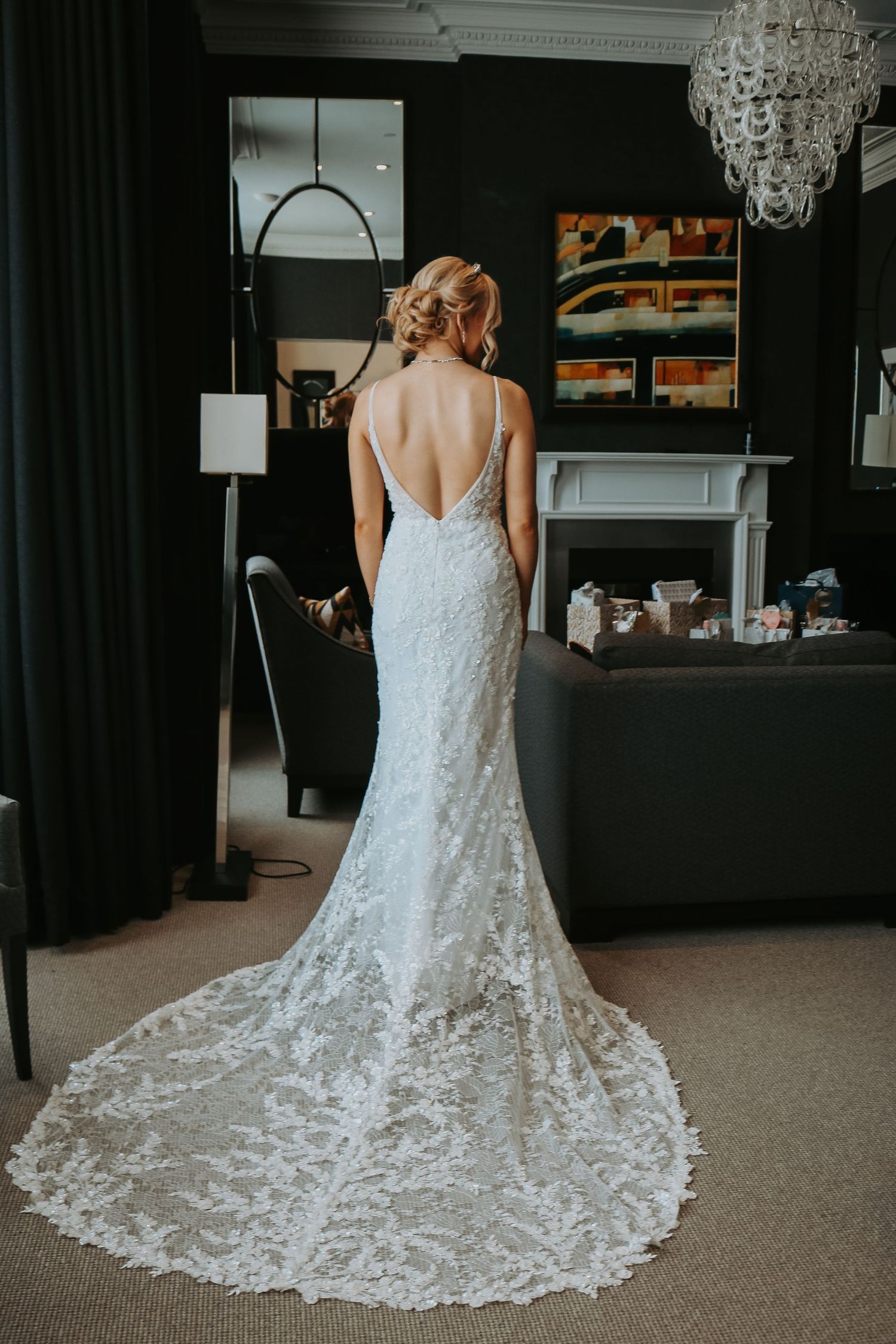 Back view of an elegant lace wedding dress with a dramatic long train and open back detail in a modern room setting.