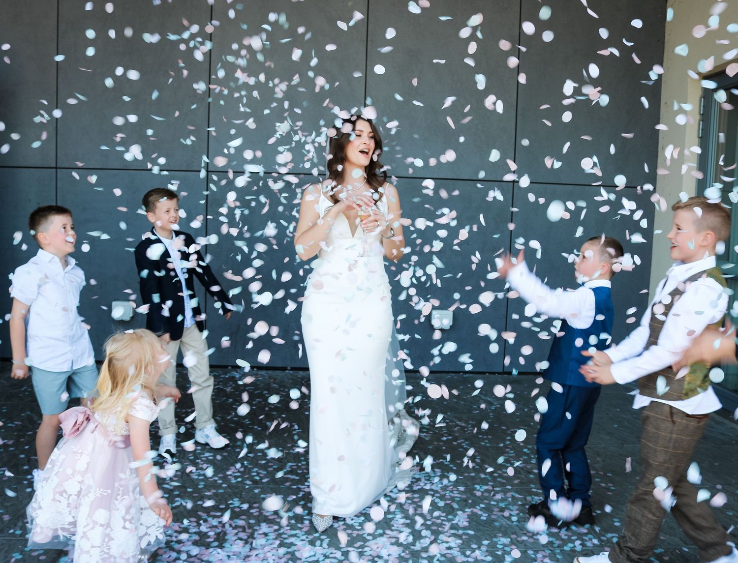 A bride and wedding party celebrate under a shower of white confetti outside in a magical joyful moment.