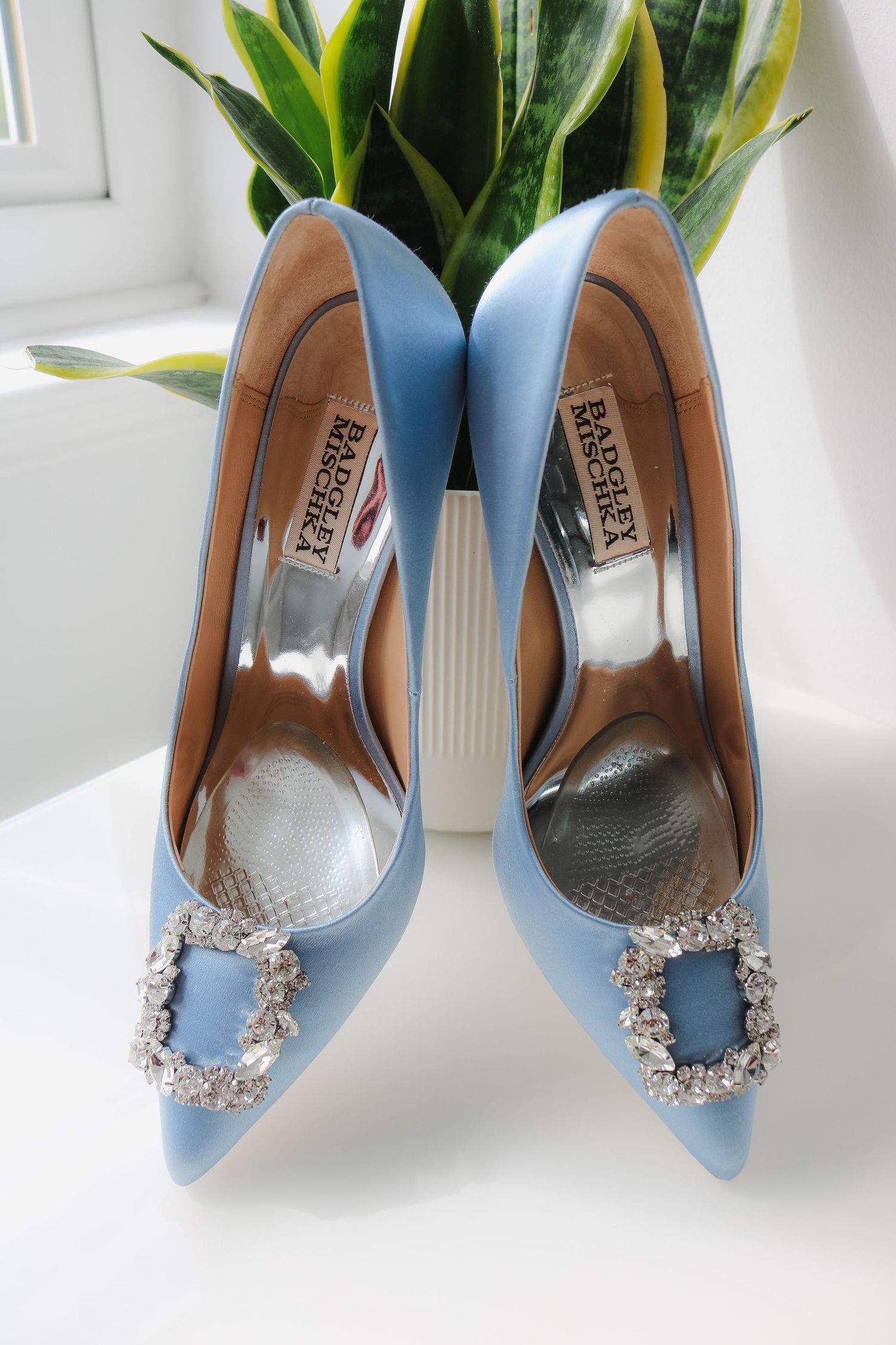 Light blue satin pumps with crystal embellished buckles displayed from different angles against a white background.