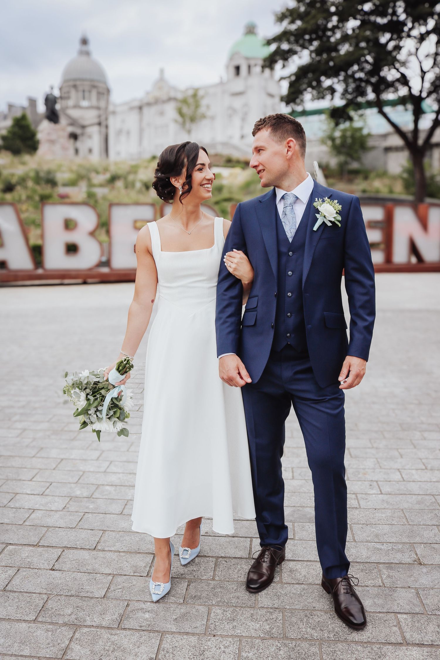 A wedding couple poses outside in Aberdeen, Scotland, with historic architecture and city signage visible in the background.