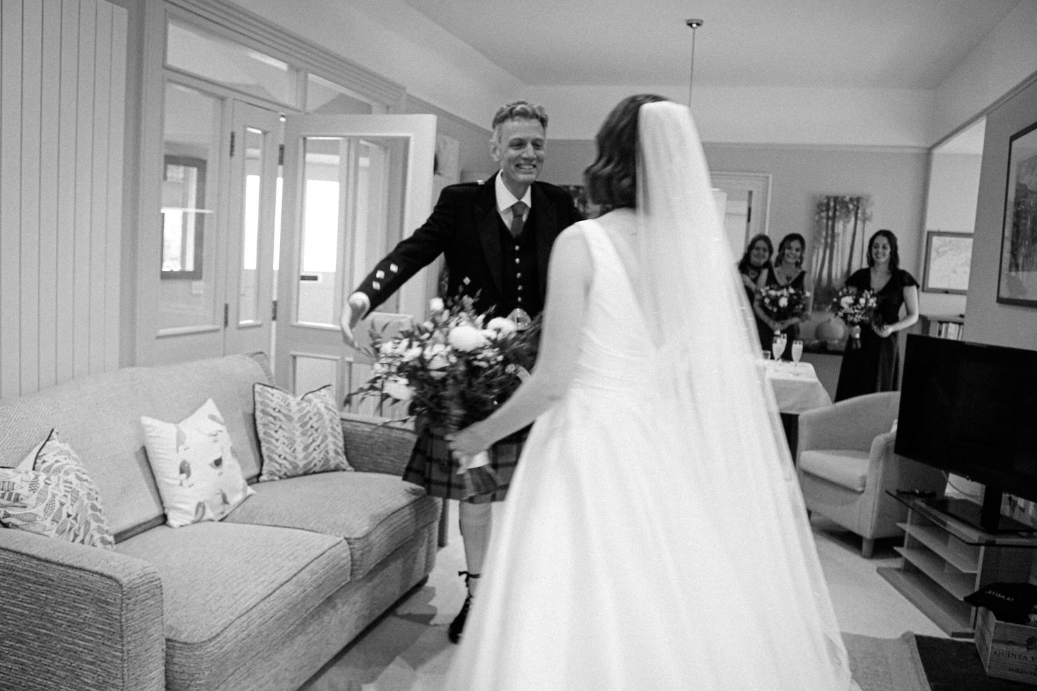 Tender moment captured at a wedding celebration in a bright interior living room setting with a modern grey couch.