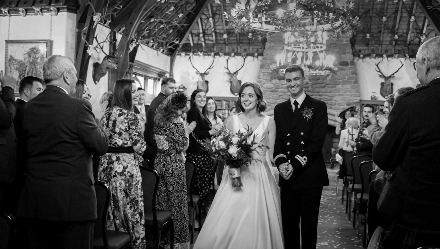 Black and white vintage photograph showing a wedding ceremony in a decorated archway with guests looking on.