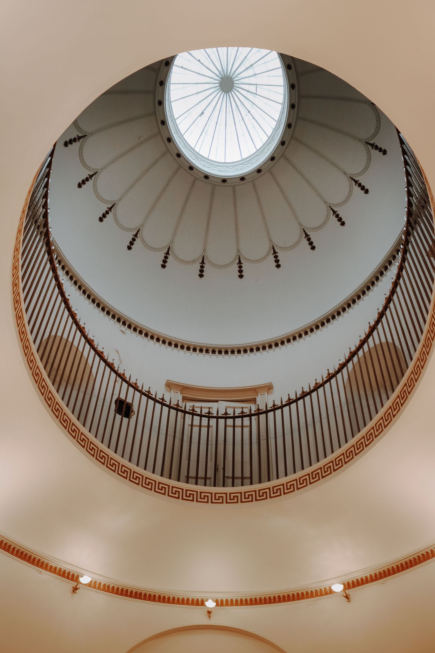Looking up at an elegant domed ceiling with circular skylight and decorative Greek key pattern trim in a classical building.