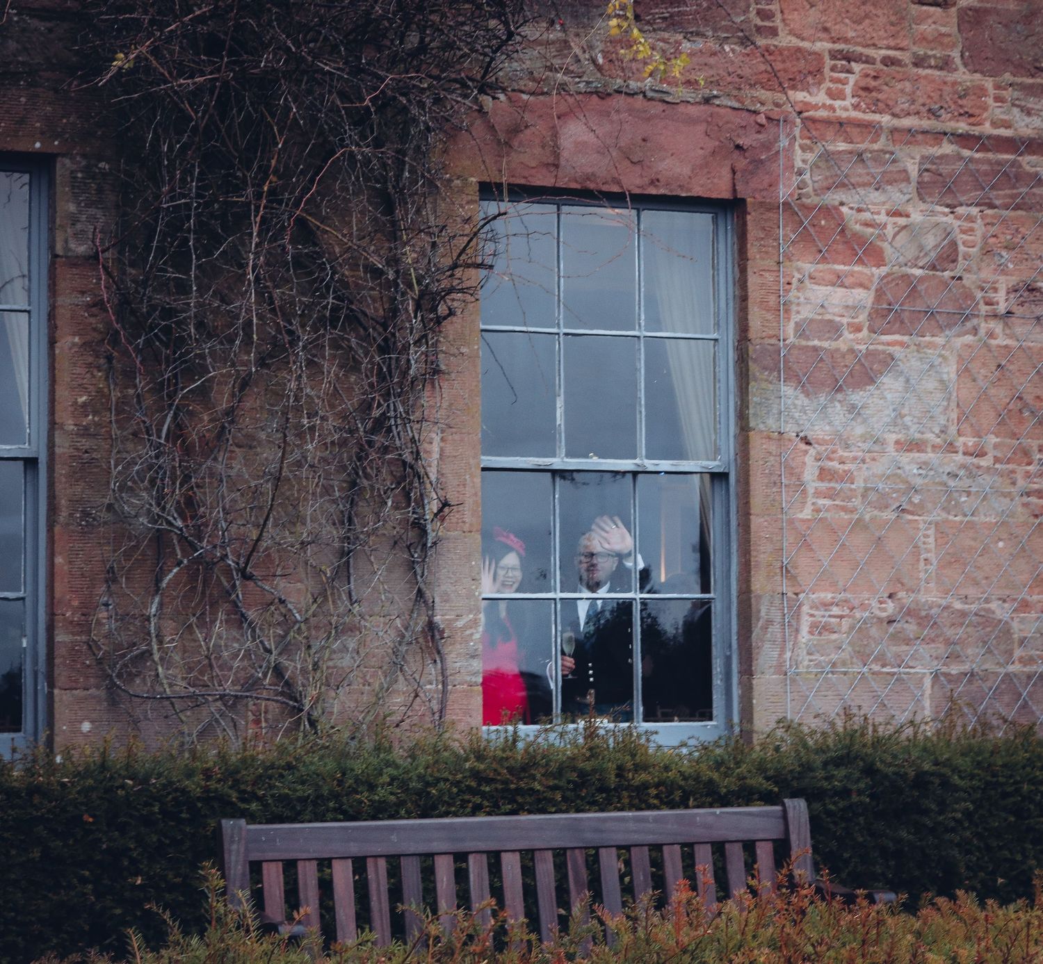 A window in an old brick building with dead vines and a wooden bench below.