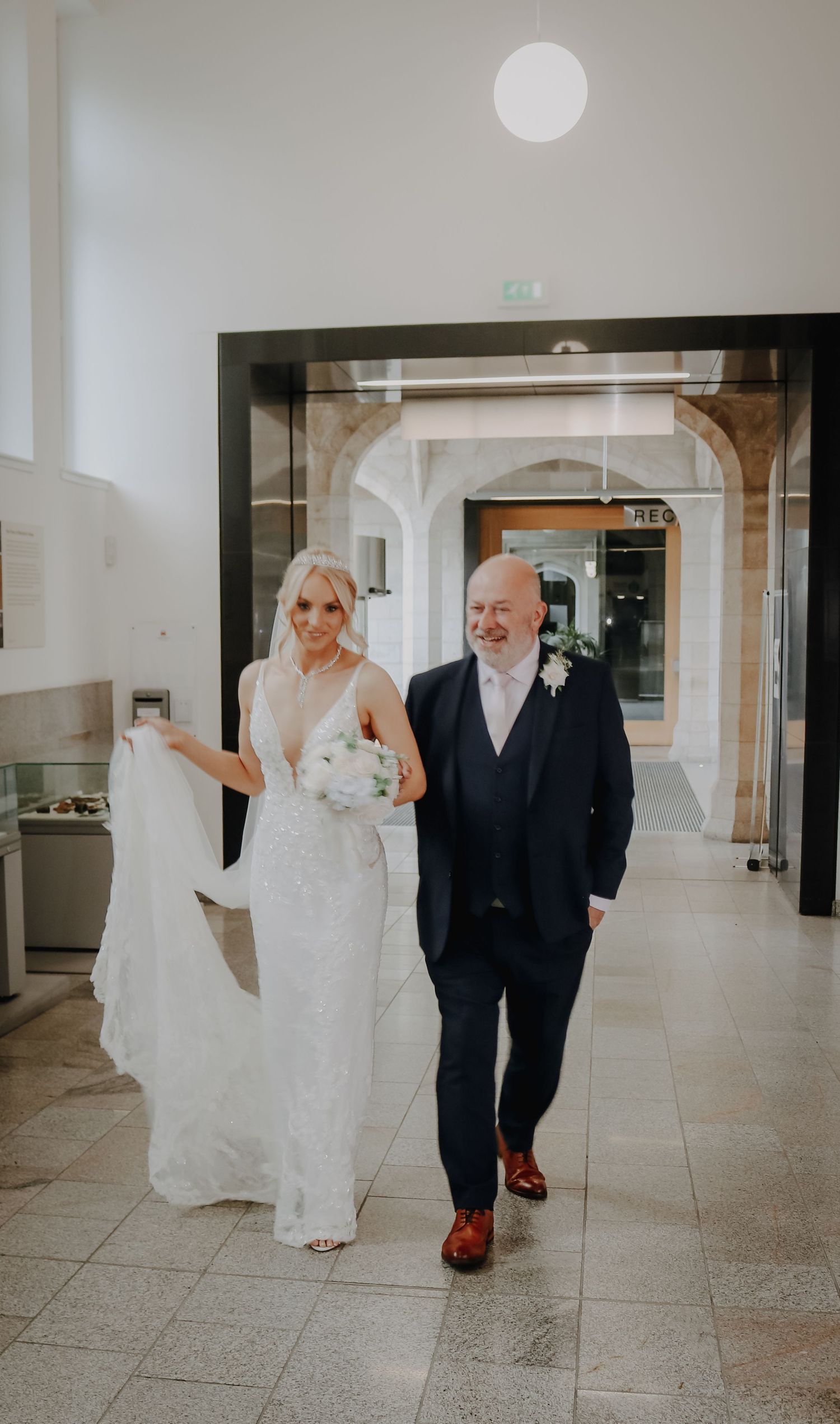 A couple walks down an elegant hallway on their wedding day with white decor and architectural details.