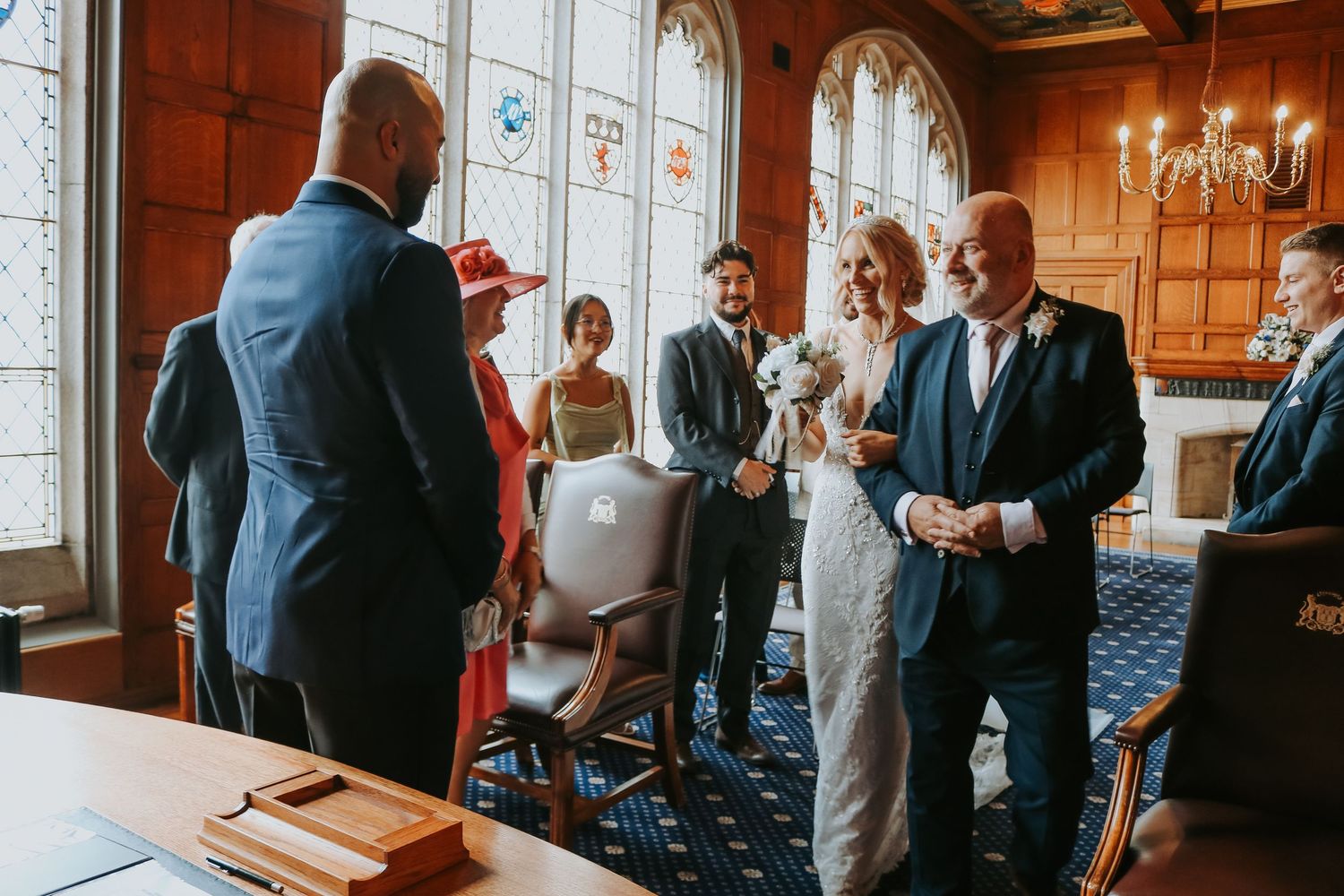 Wedding ceremony guests gather in an elegant room with arched windows and chandelier at a historic venue.