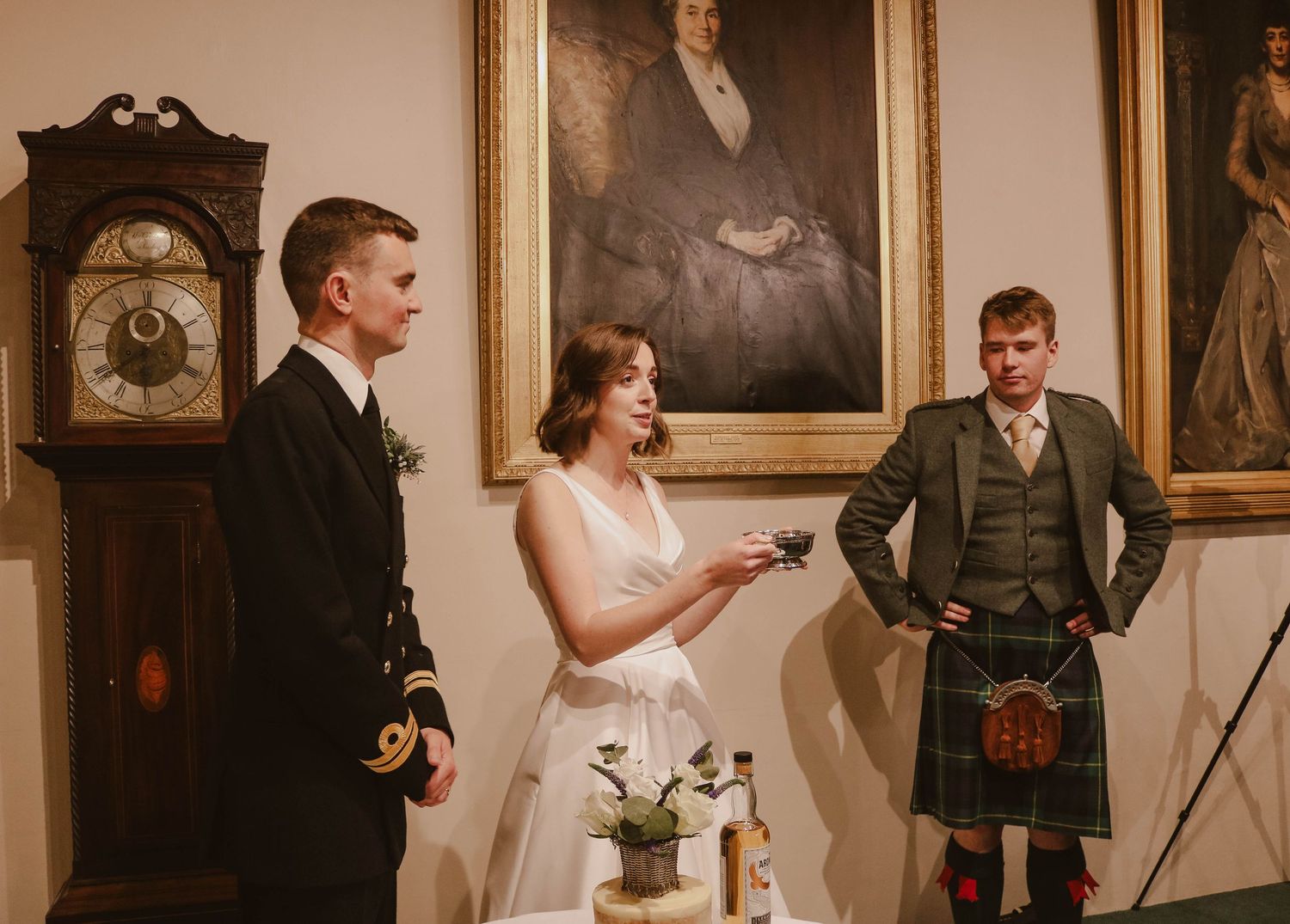 A wedding ceremony takes place in a room with vintage portraits and a grandfather clock on display.