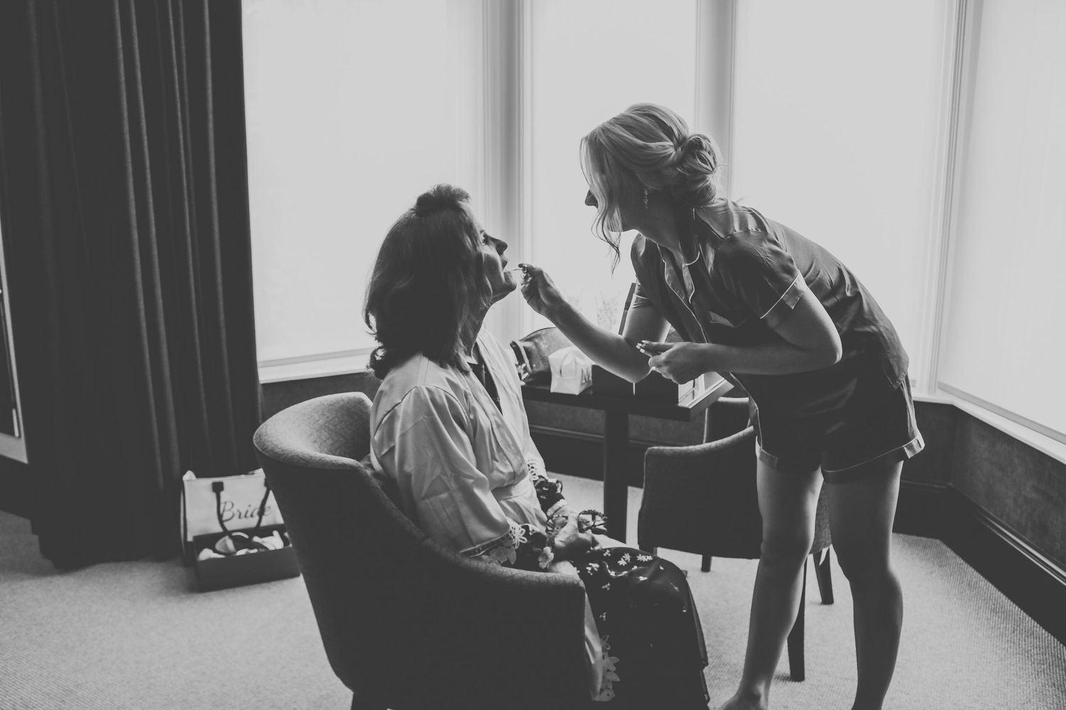Black and white photo of makeup being professionally applied in a bright modern dressing room or studio setting.
