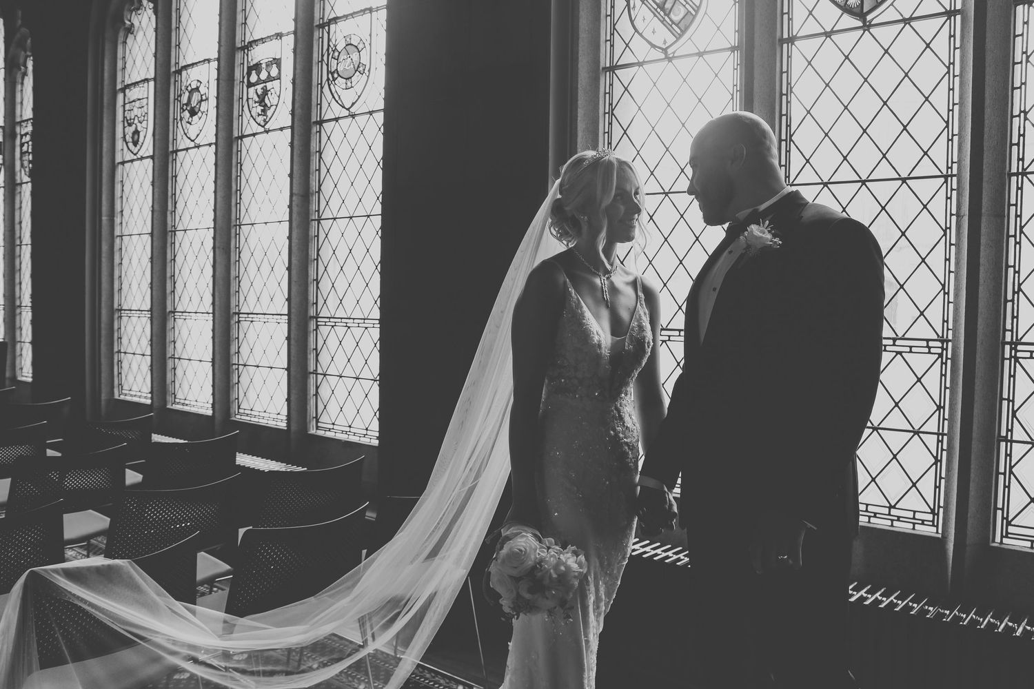 Black and white photo of newlyweds in silhouette against ornate stained glass windows.