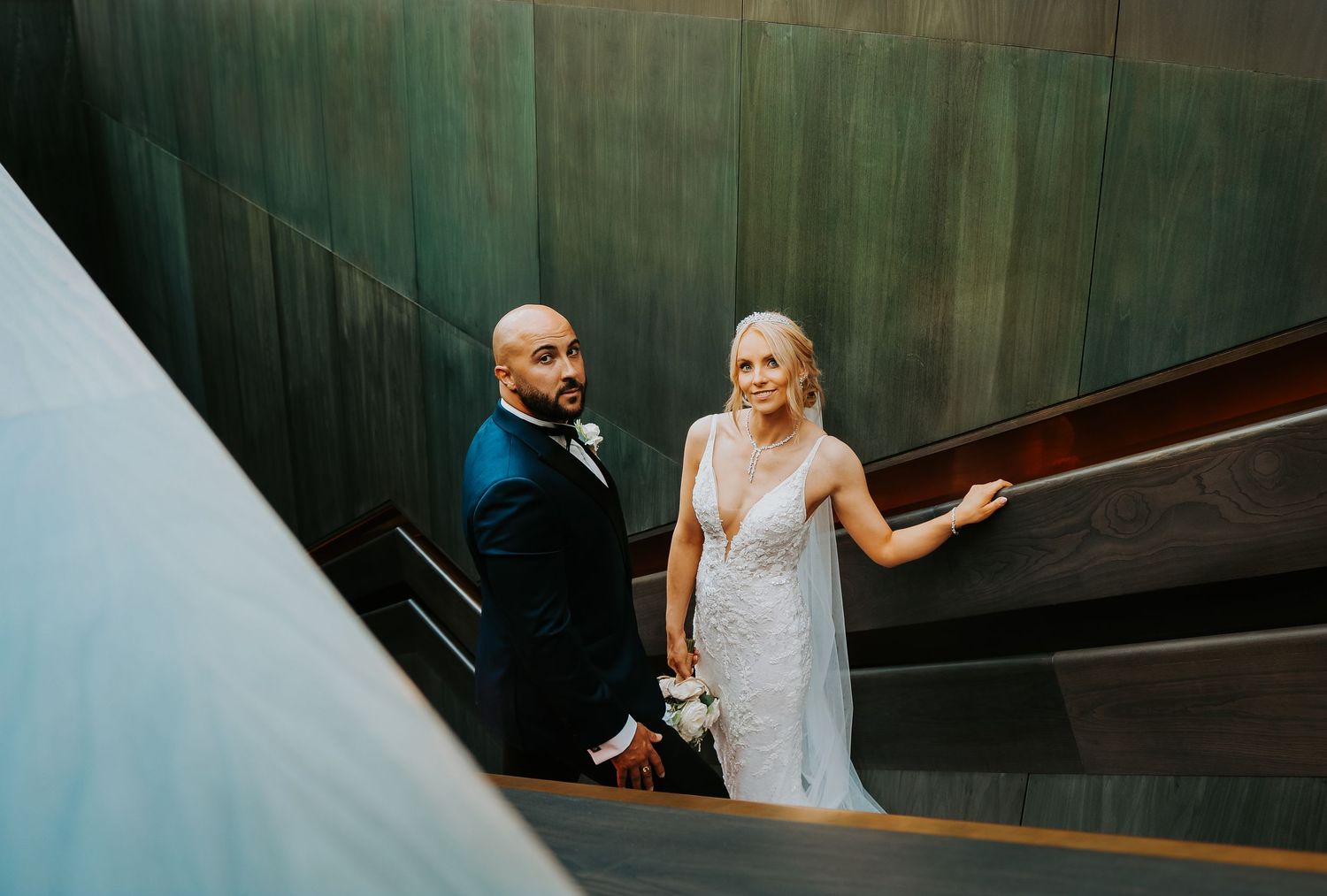 A couple shares a moment on a modern staircase in formal attire during their wedding day.