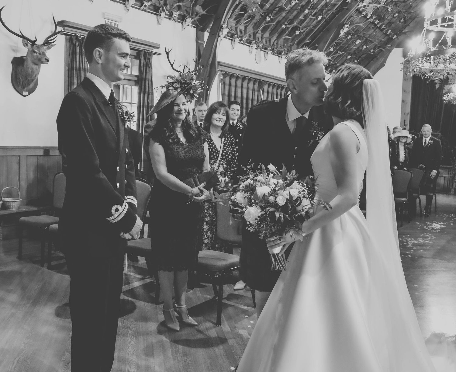 A vintage black and white wedding ceremony scene showing people gathered outdoors with a bride in an elegant satin gown.