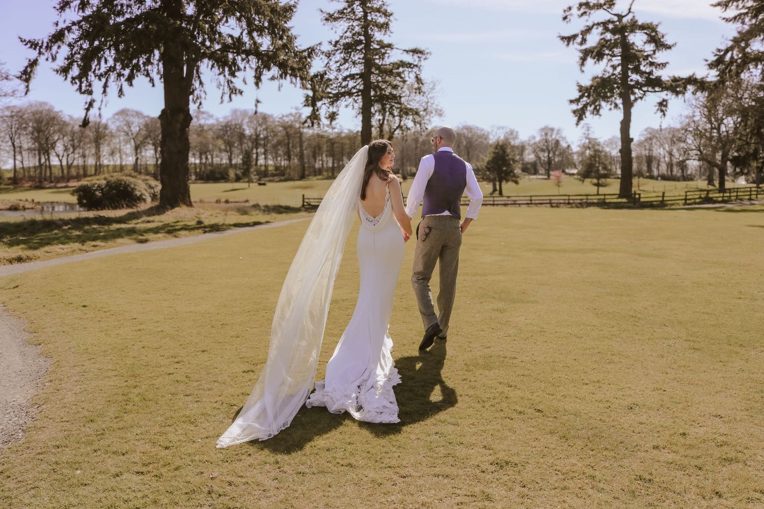 A couple shares an intimate moment on a sunny golf course as the bride's long veil flows behind her white dress.