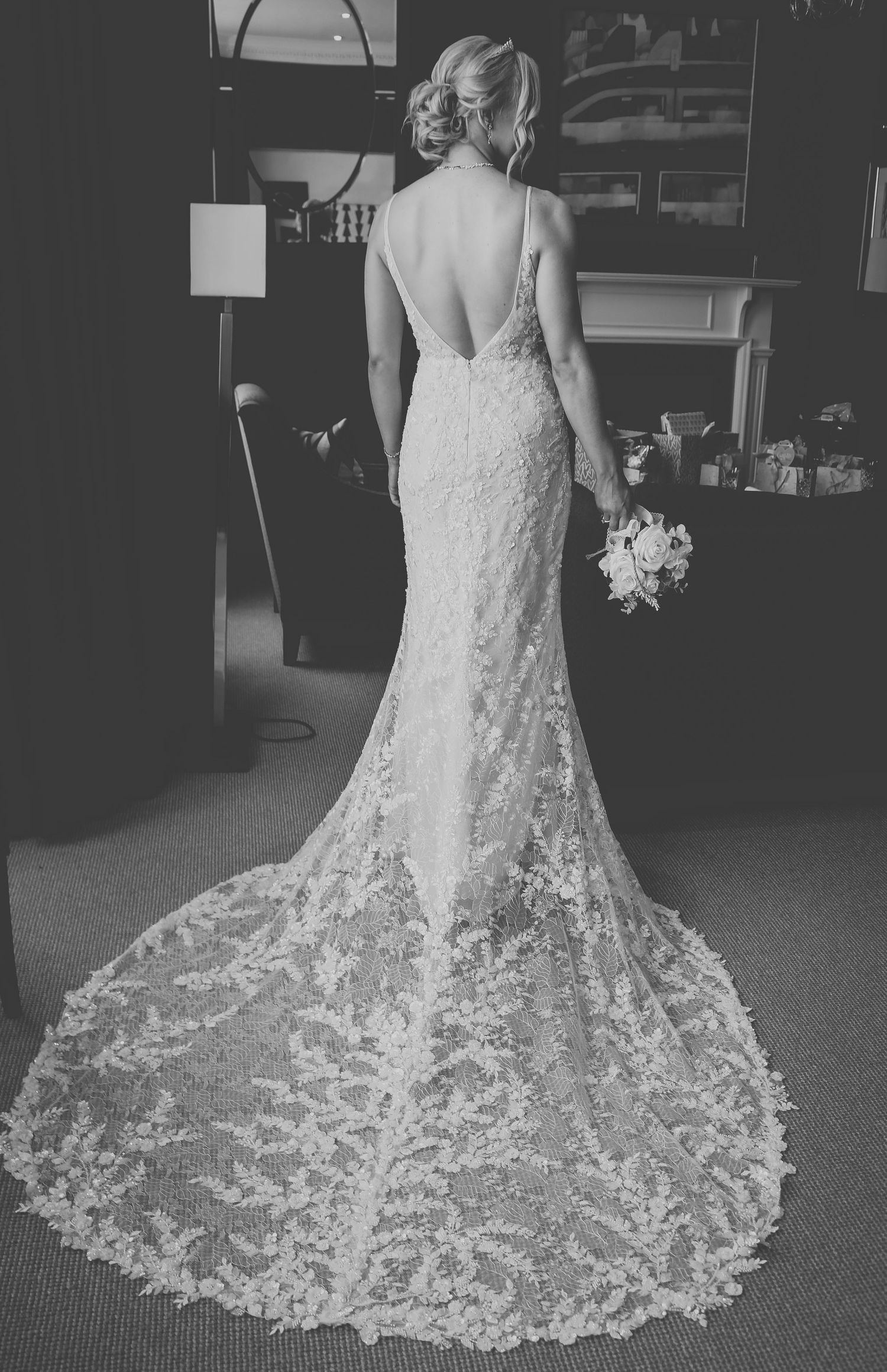 A stunning lace wedding dress with a dramatic train and plunging back is photographed in black and white.