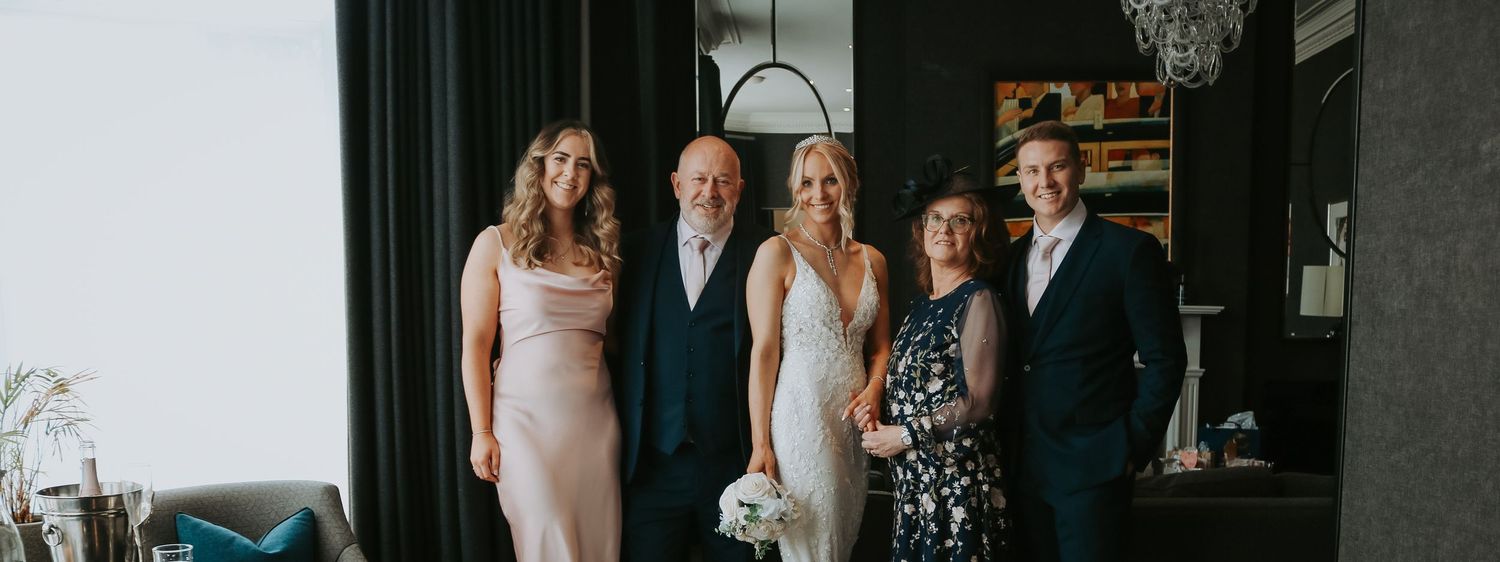 A group of wedding guests pose together in formal attire at an indoor gathering.