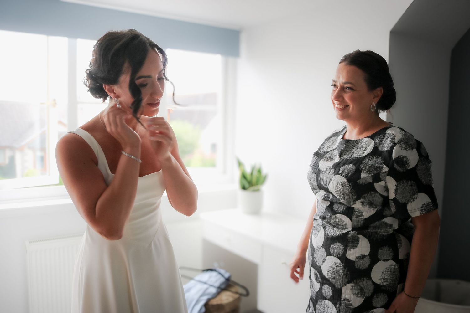 A series of candid lifestyle photos showing someone with an updo hairstyle in a black and white floral dress by a window.