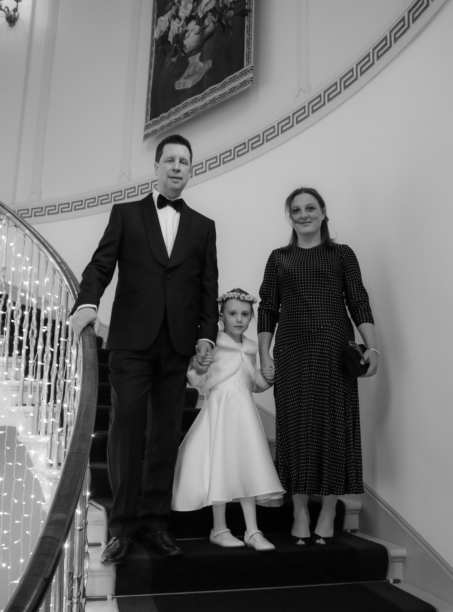 Black and white formal portrait of a family of three posing on an elegant staircase with decorative railings.