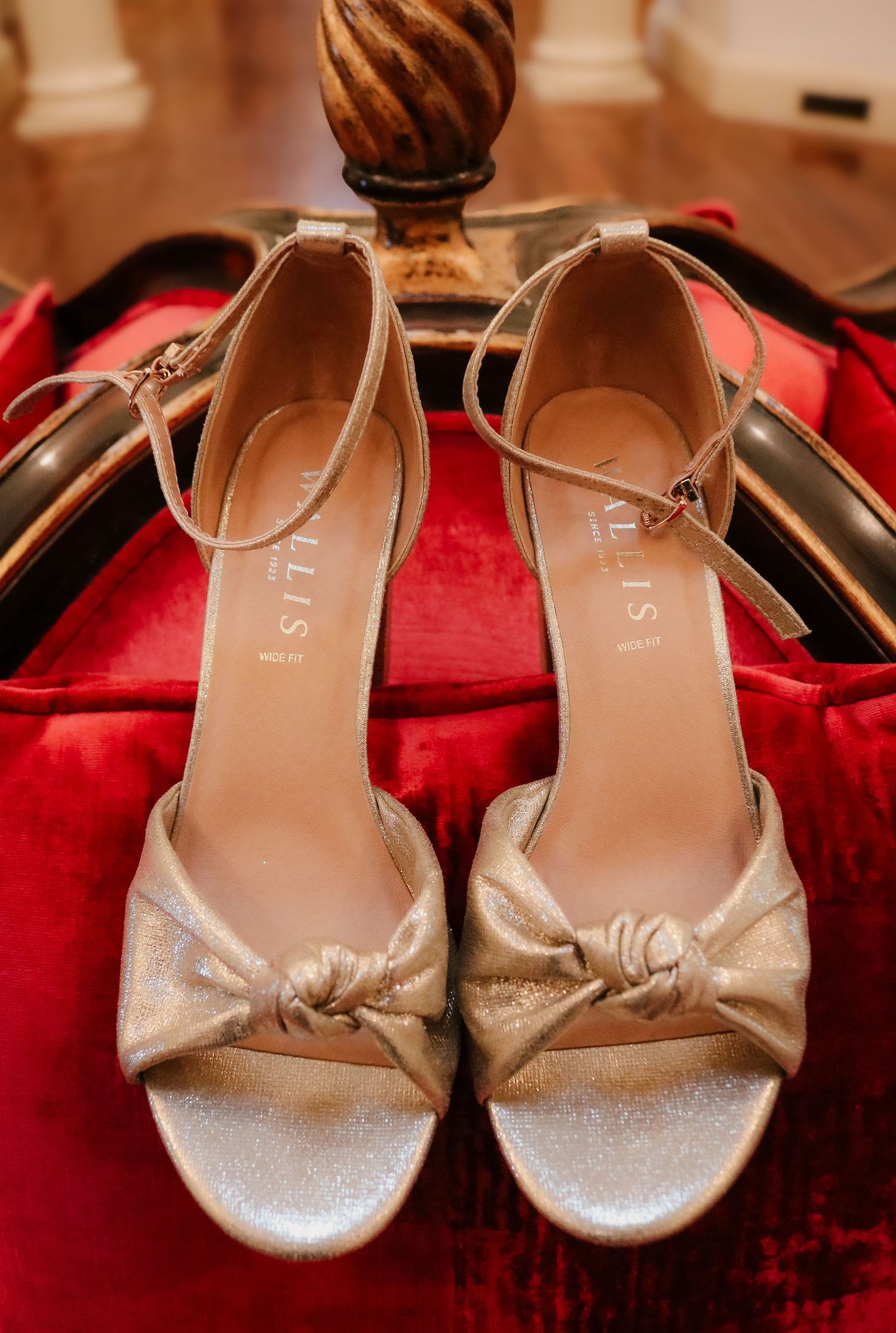 Elegant gold metallic bridal sandals with knotted detail displayed on red velvet surface.