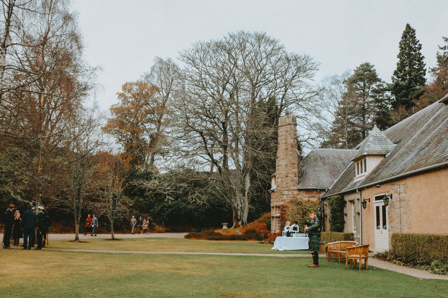 Rustic stone church with pink cottage and autumn trees on spacious lawn in Scotland.