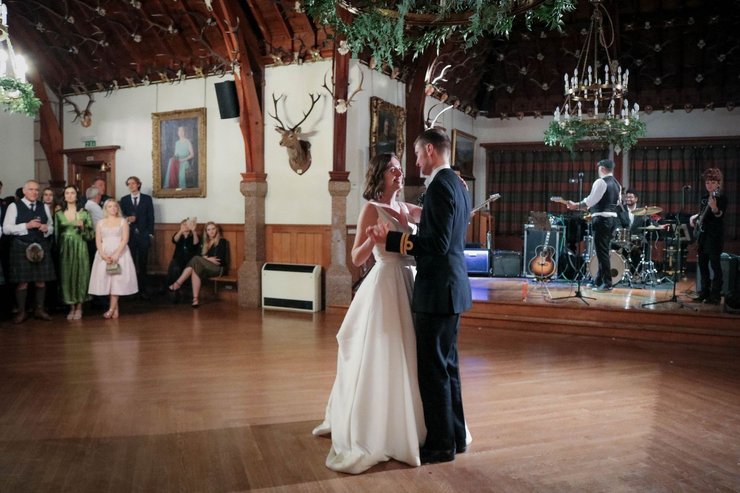 A couple shares their first dance on a hardwood floor at a rustic lodge venue with mounted deer antlers on the wall.