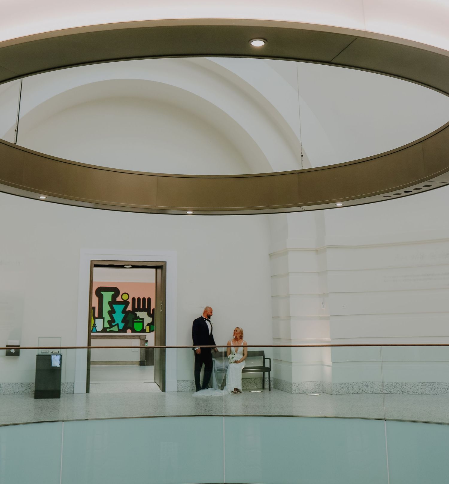 Wedding couple standing on a modern circular balcony overlooking an interior space with minimalist architecture.