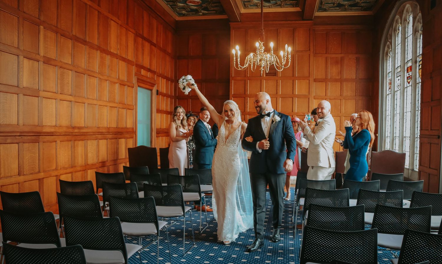 A celebratory moment inside a wood-paneled room with elegant chandelier and rows of chairs during a special occasion.