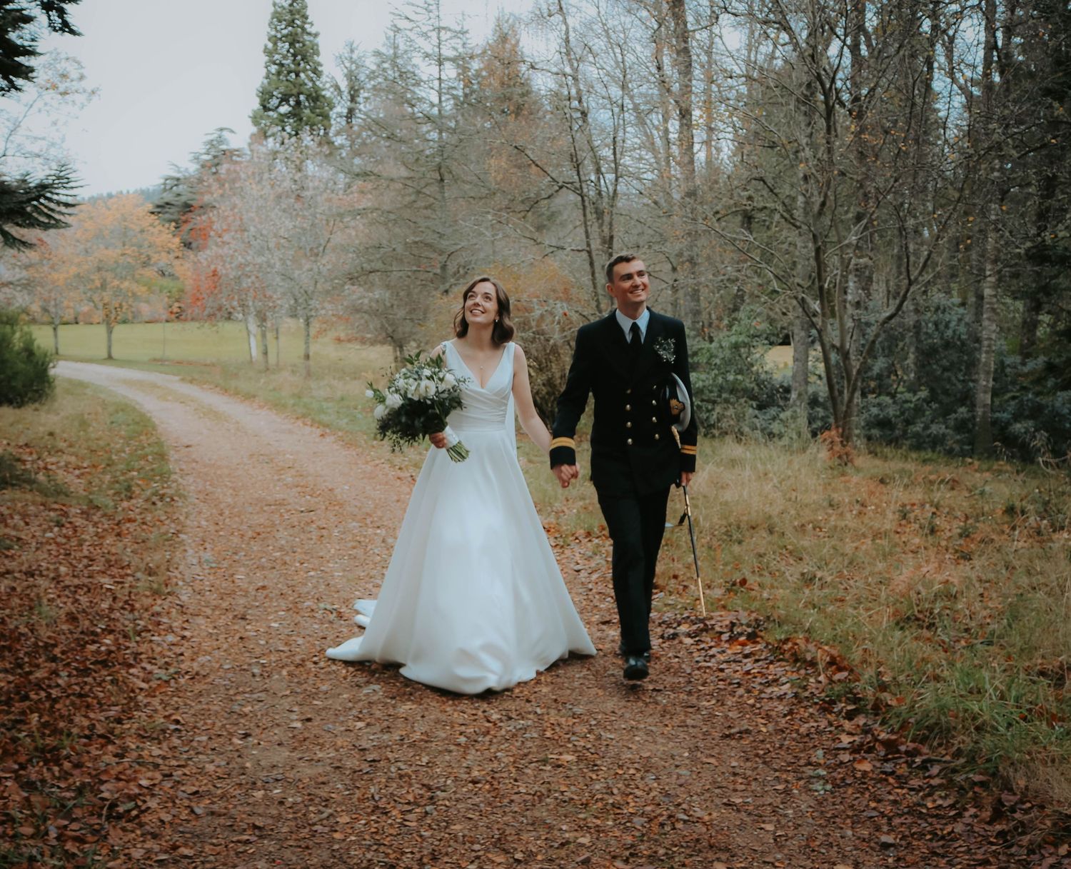 A couple walks hand in hand along an autumn forest path during their wedding celebration.