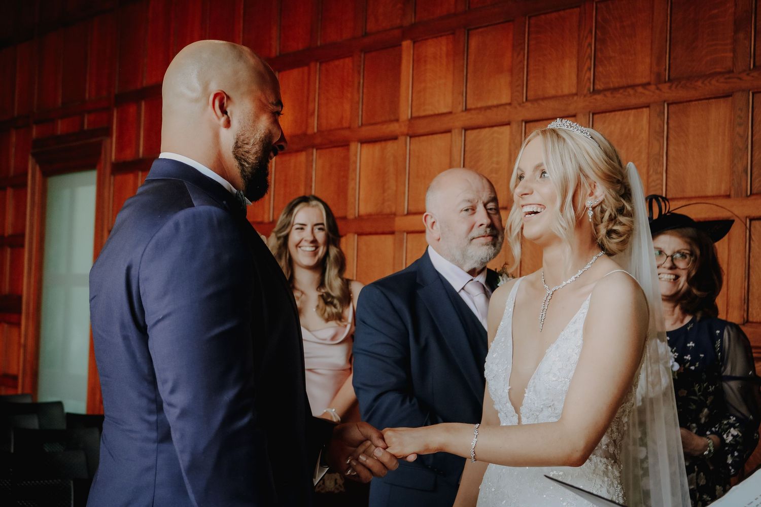 Happy bride and groom share a touching moment during their wedding ceremony in a wood-paneled venue.