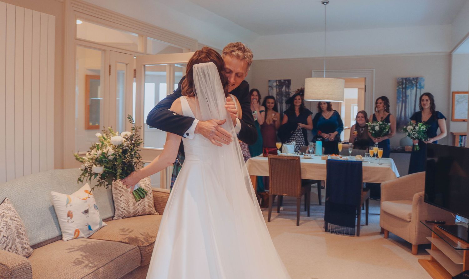 A couple shares their first dance at a wedding reception while guests look on in the background.