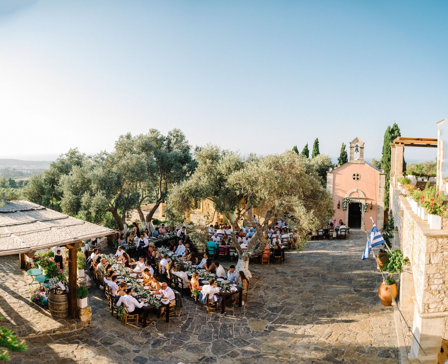 A panoramic view of an outdoor wedding reception at Agreco Farms, Crete with tables set among olive trees in a rustic Mediterranean setting.