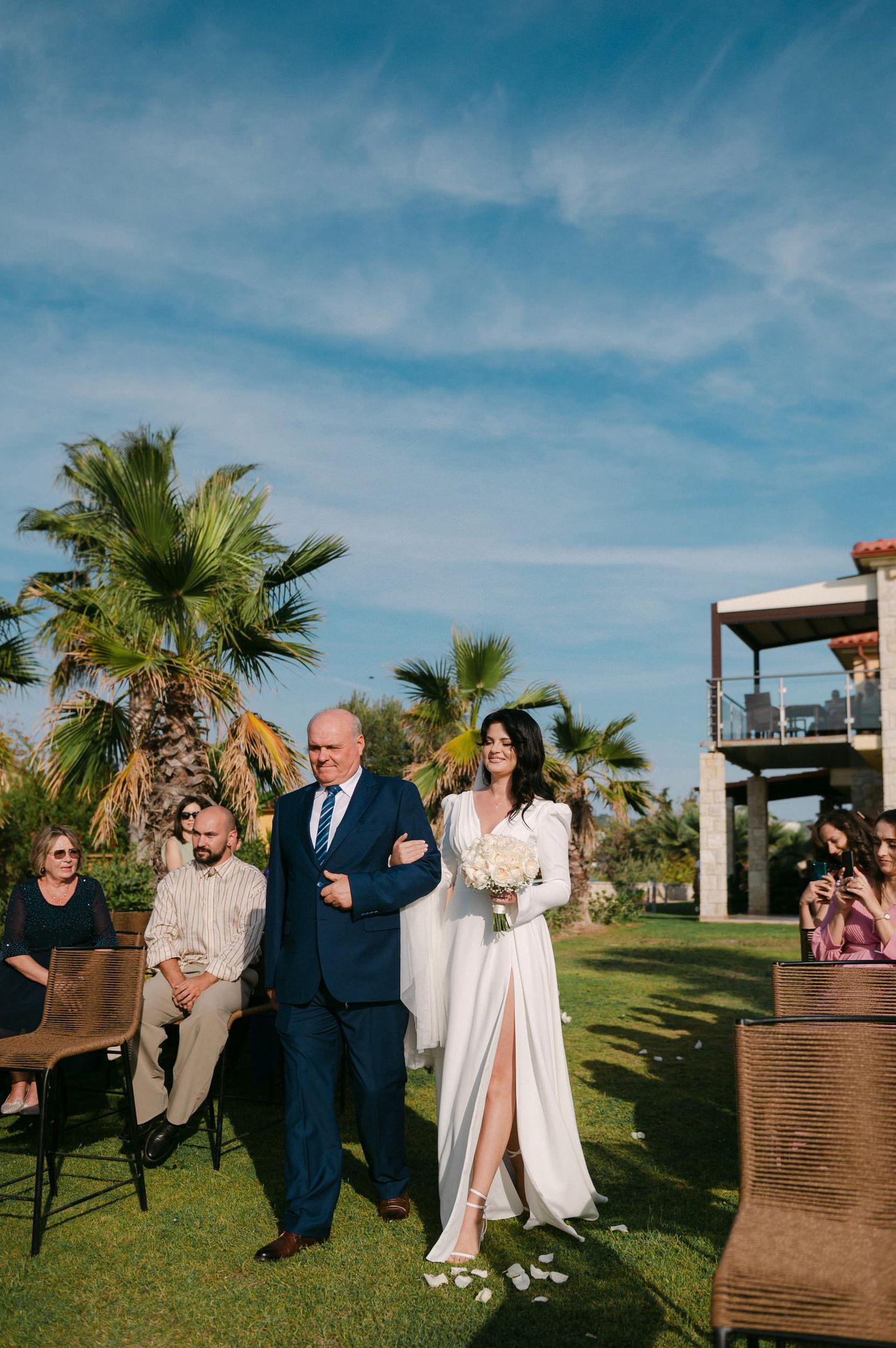 Wedding party members share joyful moments and laughter on a sunny day with palm trees in the background.