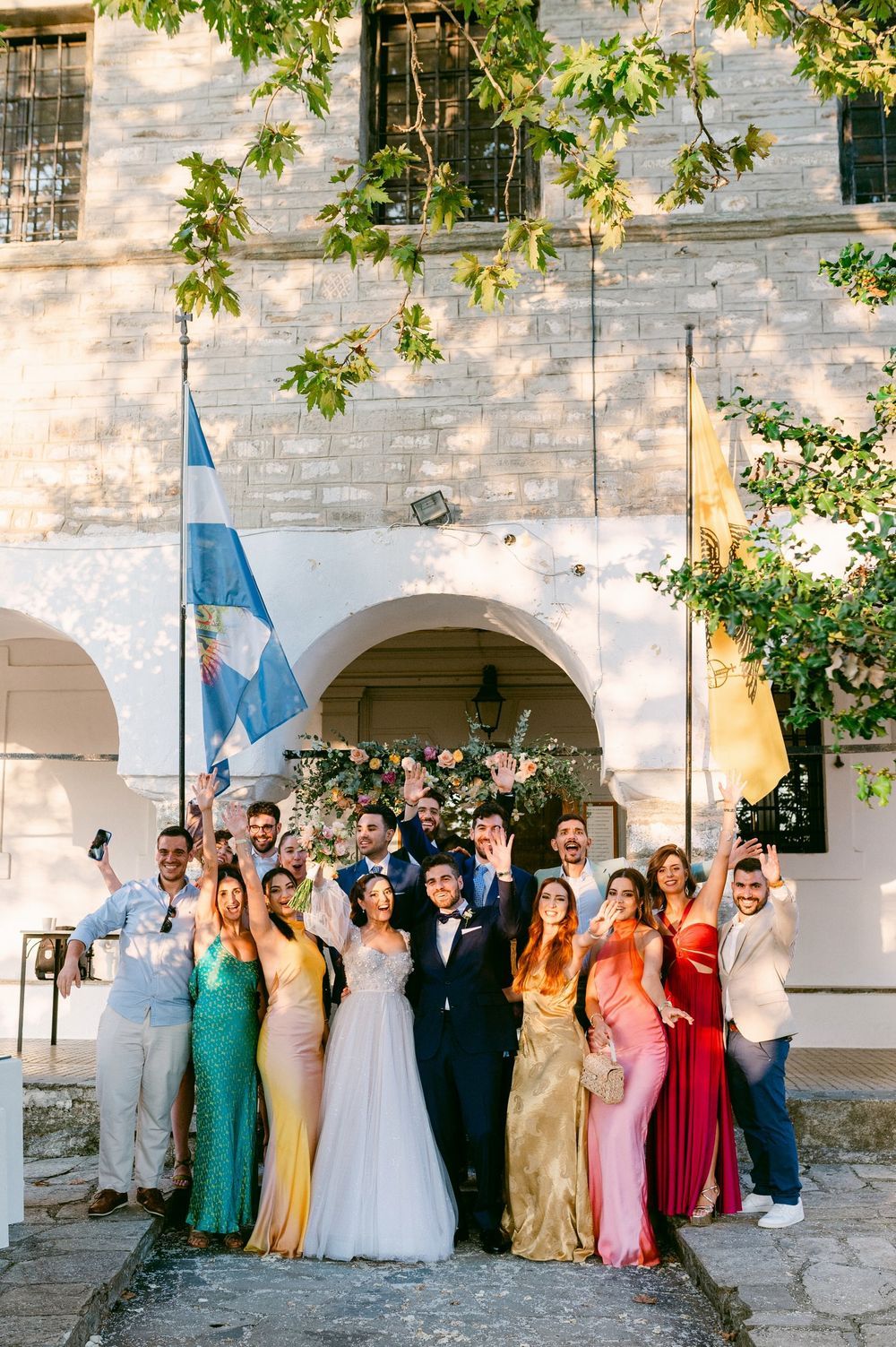 Wedding party group photo outside a stone church with colorful bridesmaid dresses and arched architecture.