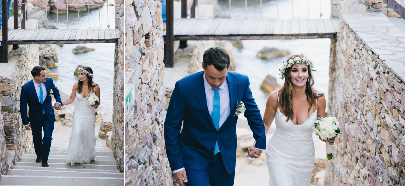 Wedding couple walking through a rustic stone archway decorated with floral arrangements.