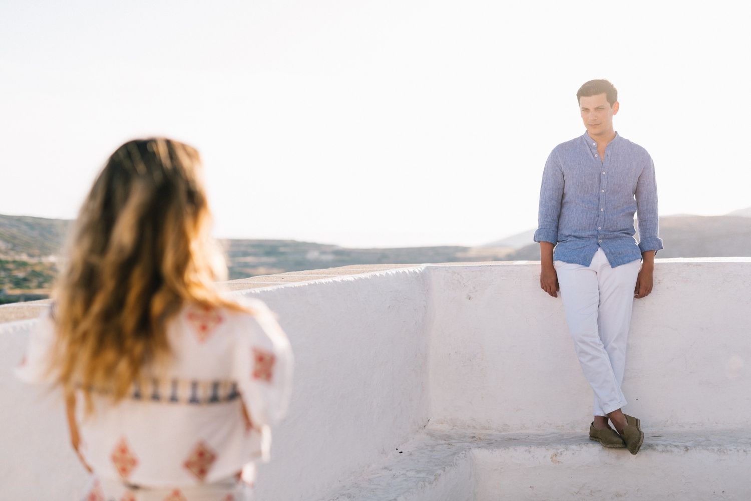 Stylish couple in casual attire poses on white terrace during sunset photoshoot.