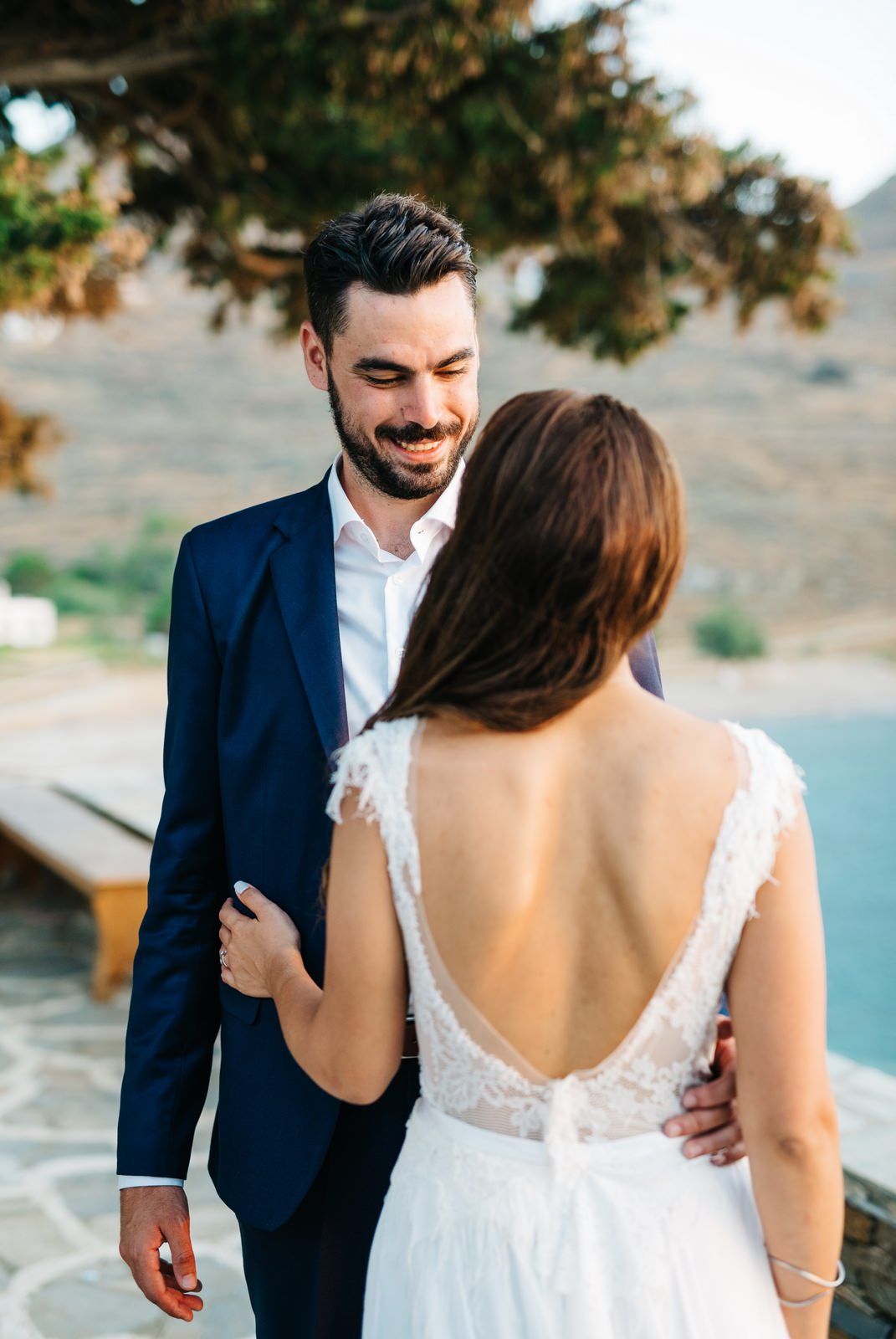 Elegant couple in wedding attire share a tender moment at a coastal venue.