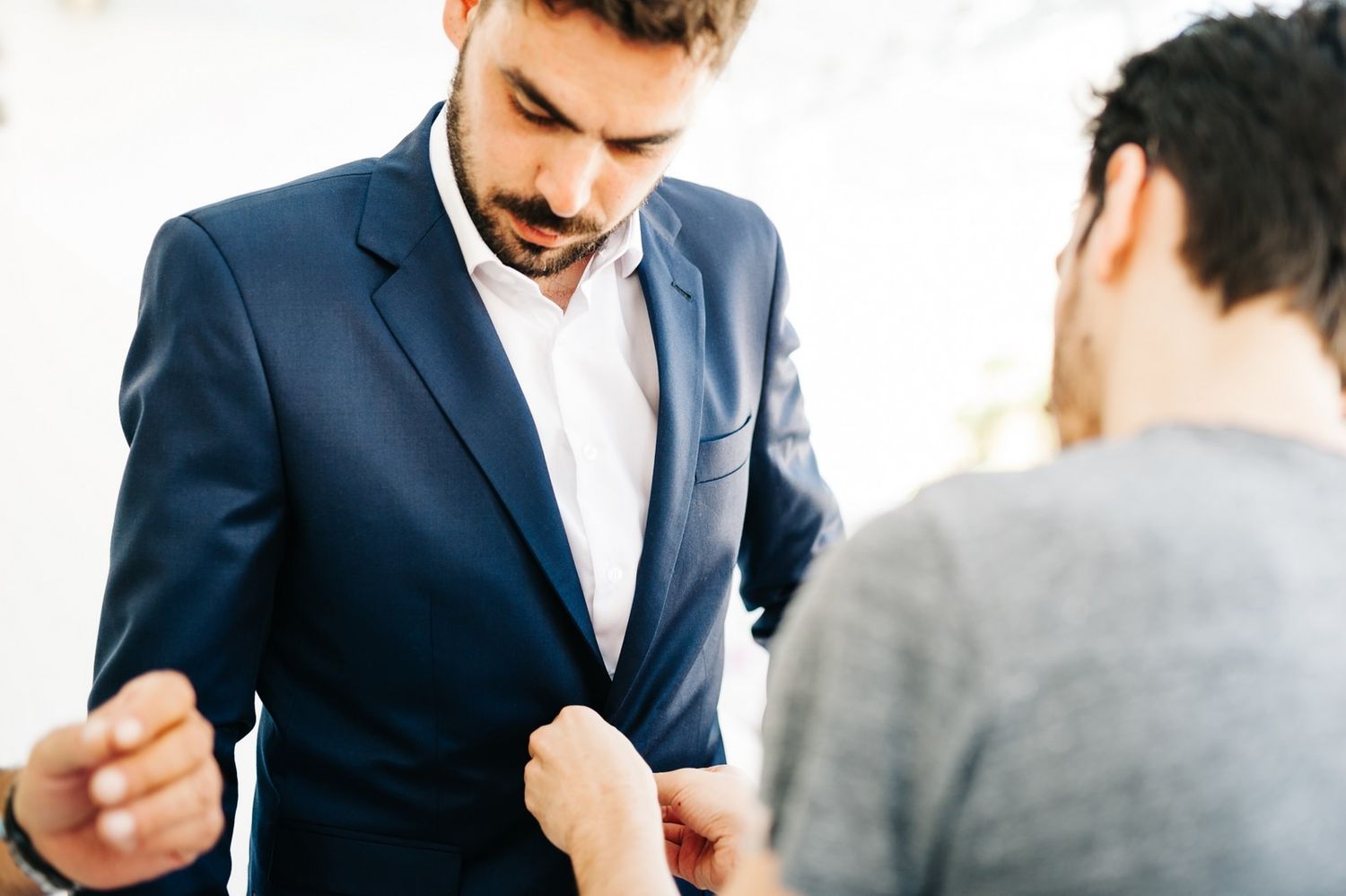 Person buttoning up a navy blue suit jacket in a professional setting.
