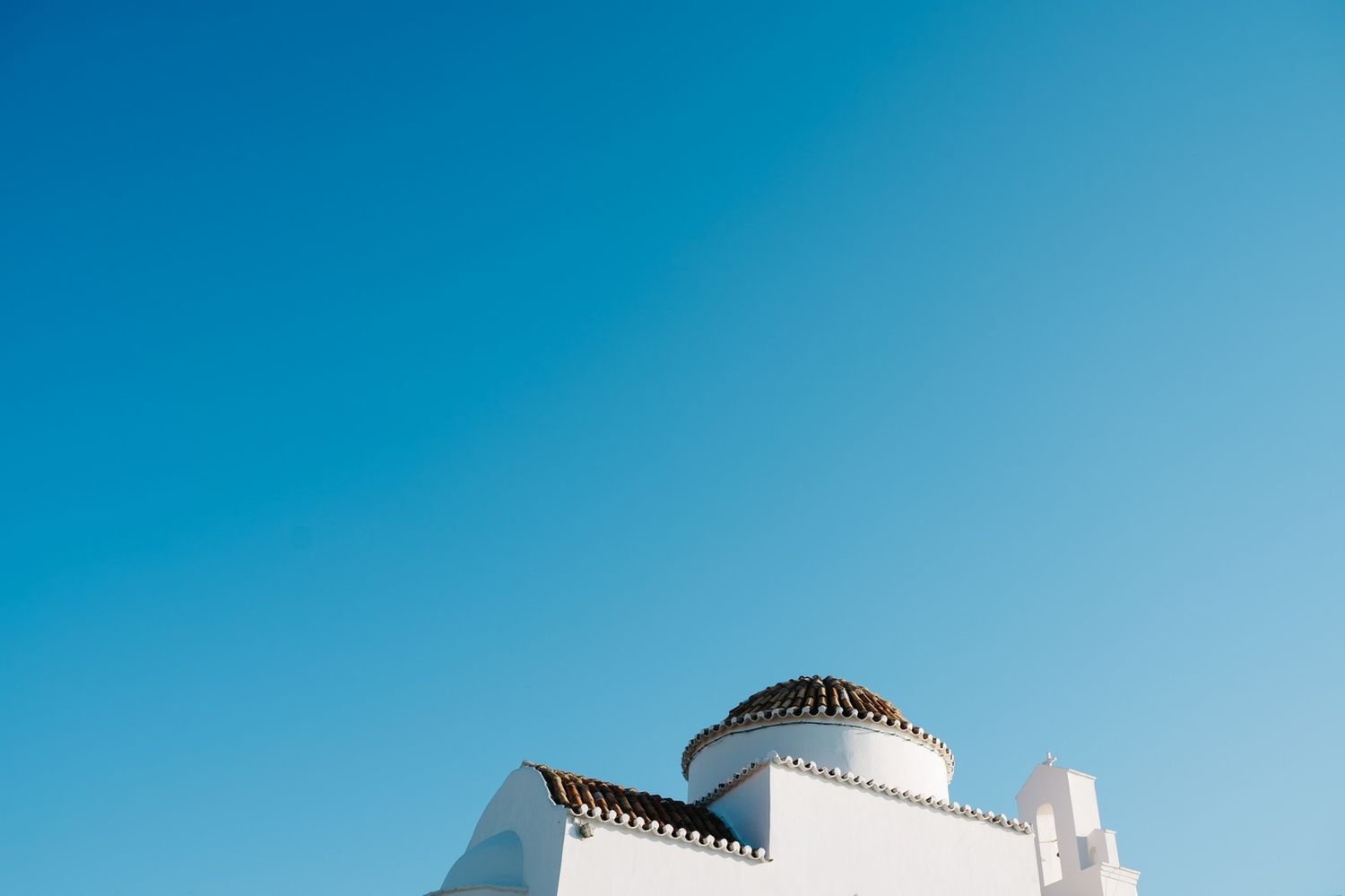 Minimalist white Mediterranean architecture with domed roof against bright blue sky.