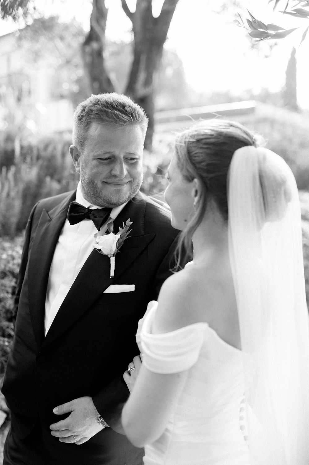 Black and white candid moment between newlyweds in formal wedding attire outdoors.