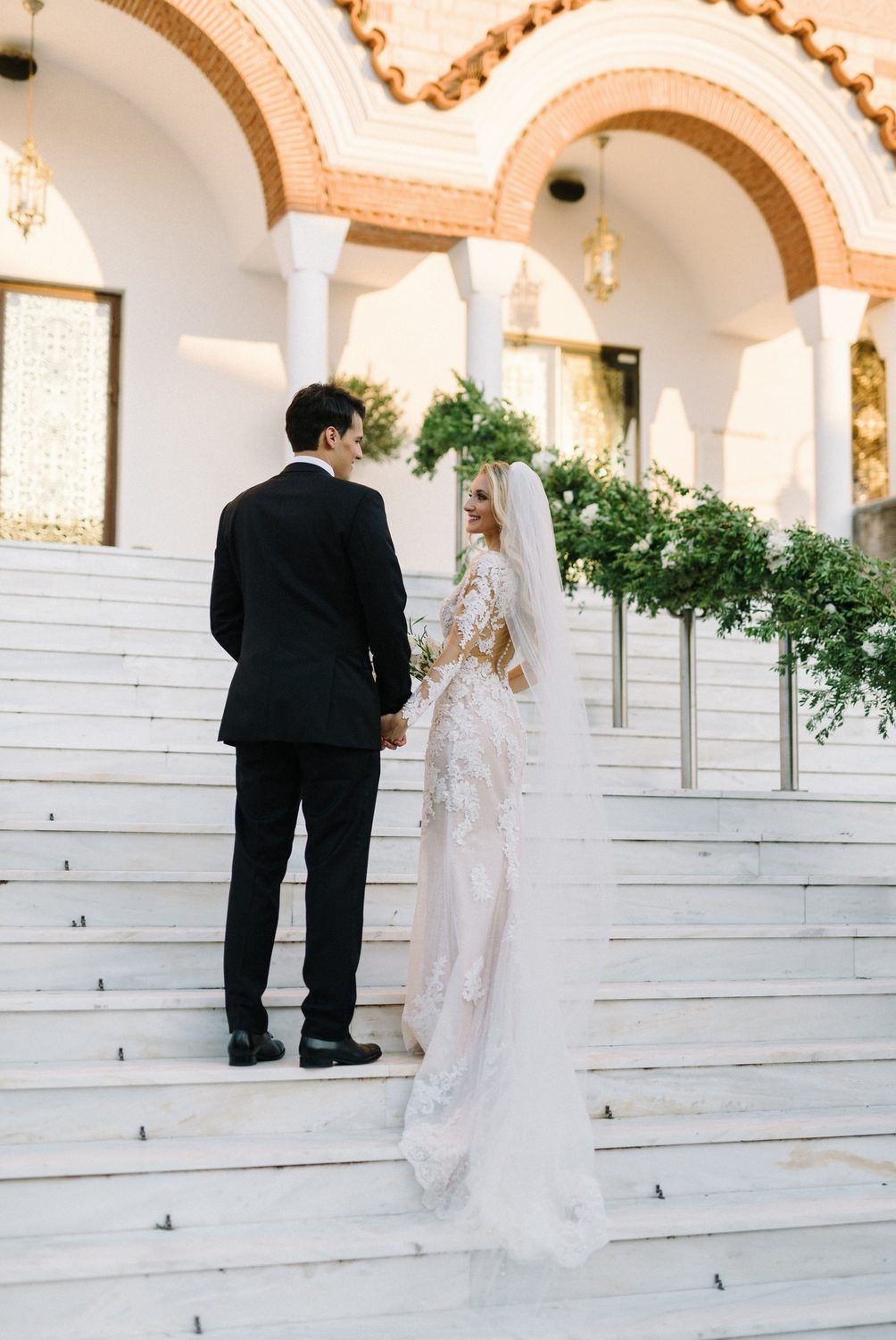 Couple standing on white marble steps under arched church architecture during wedding ceremony.