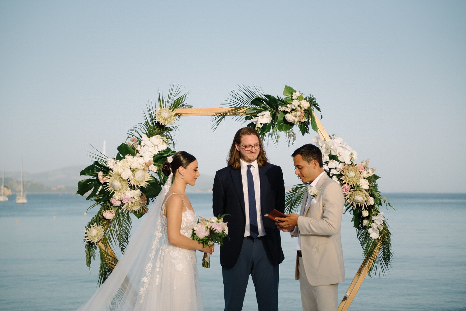 Seaside wedding ceremony under decorated arch with ocean and mountains in view.