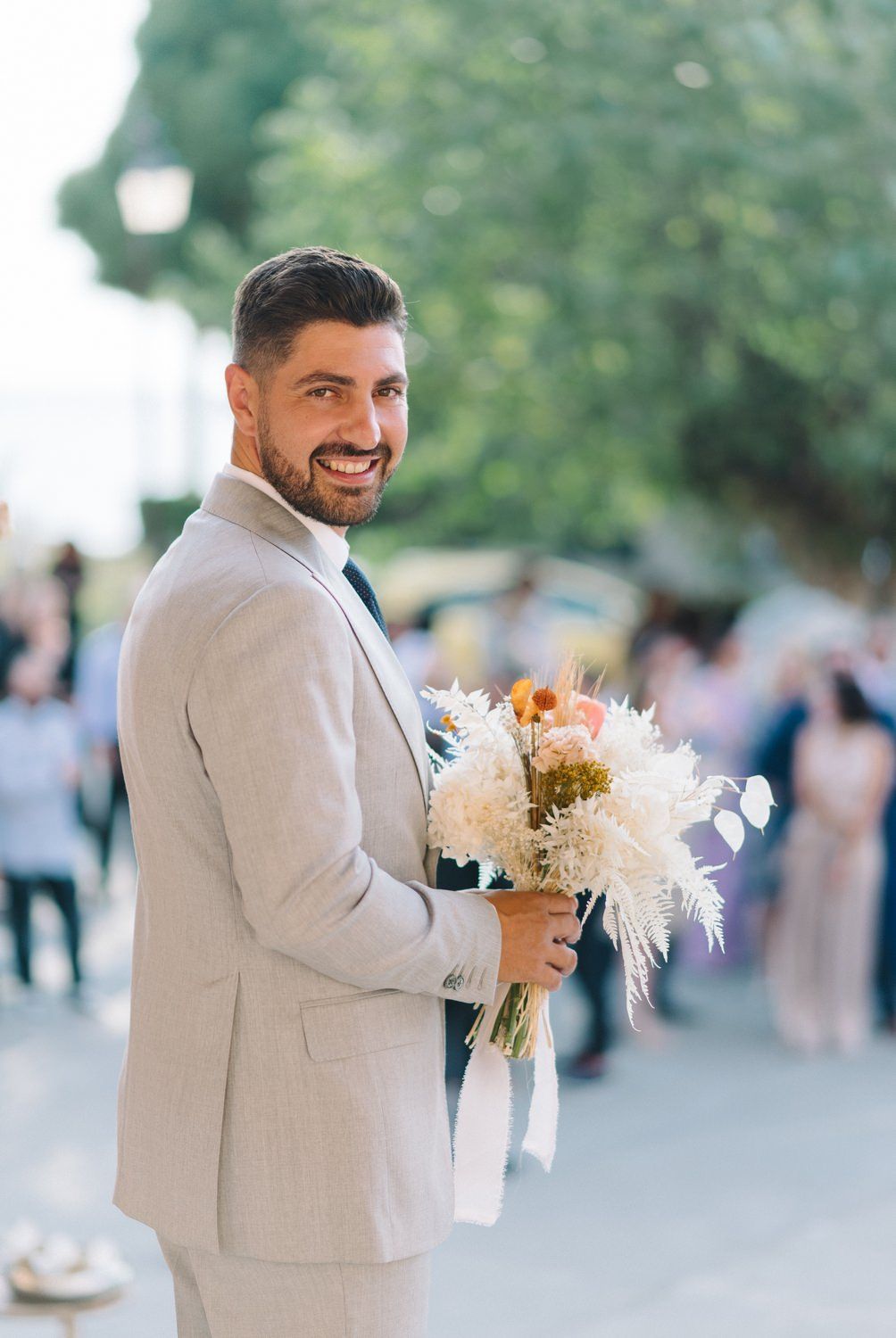 Groom in light gray suit holding romantic bouquet with pampas grass and dahlias.