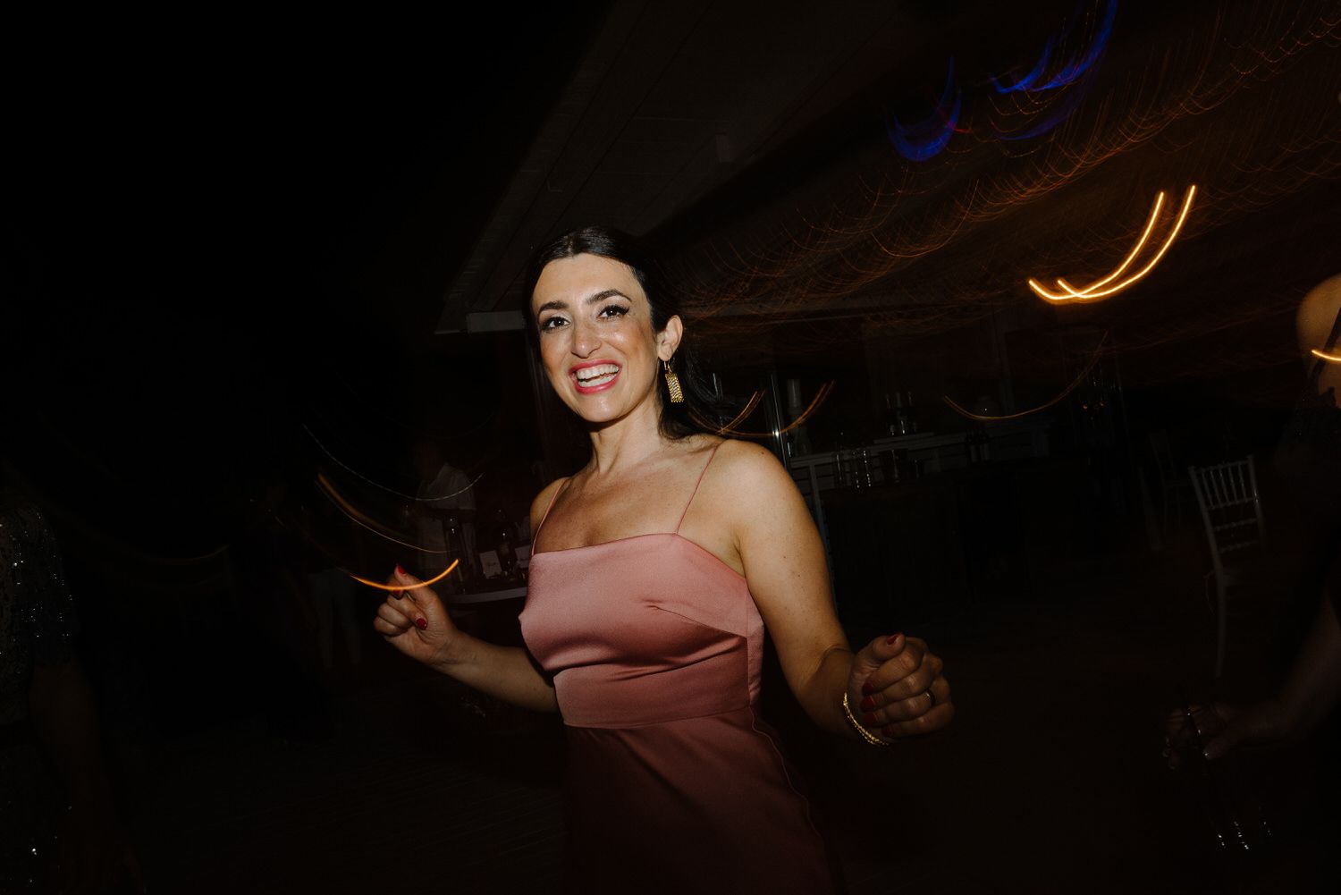 A wedding guest dances under moody lighting at an evening reception.