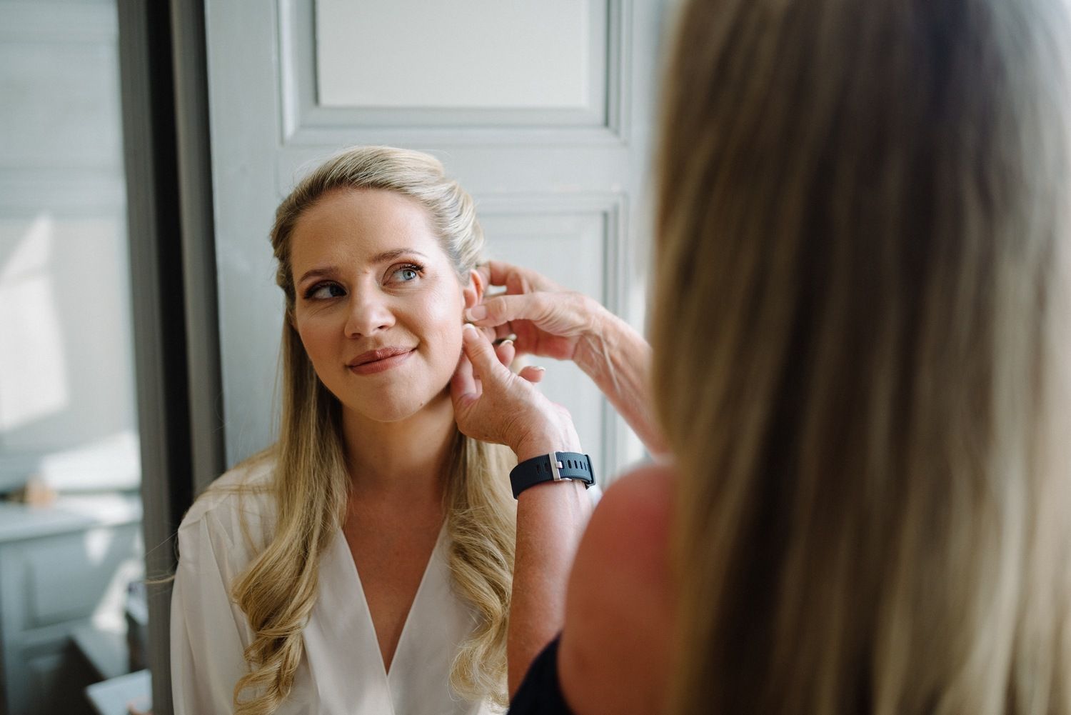 Wedding preparation moment captured by a window in natural light.