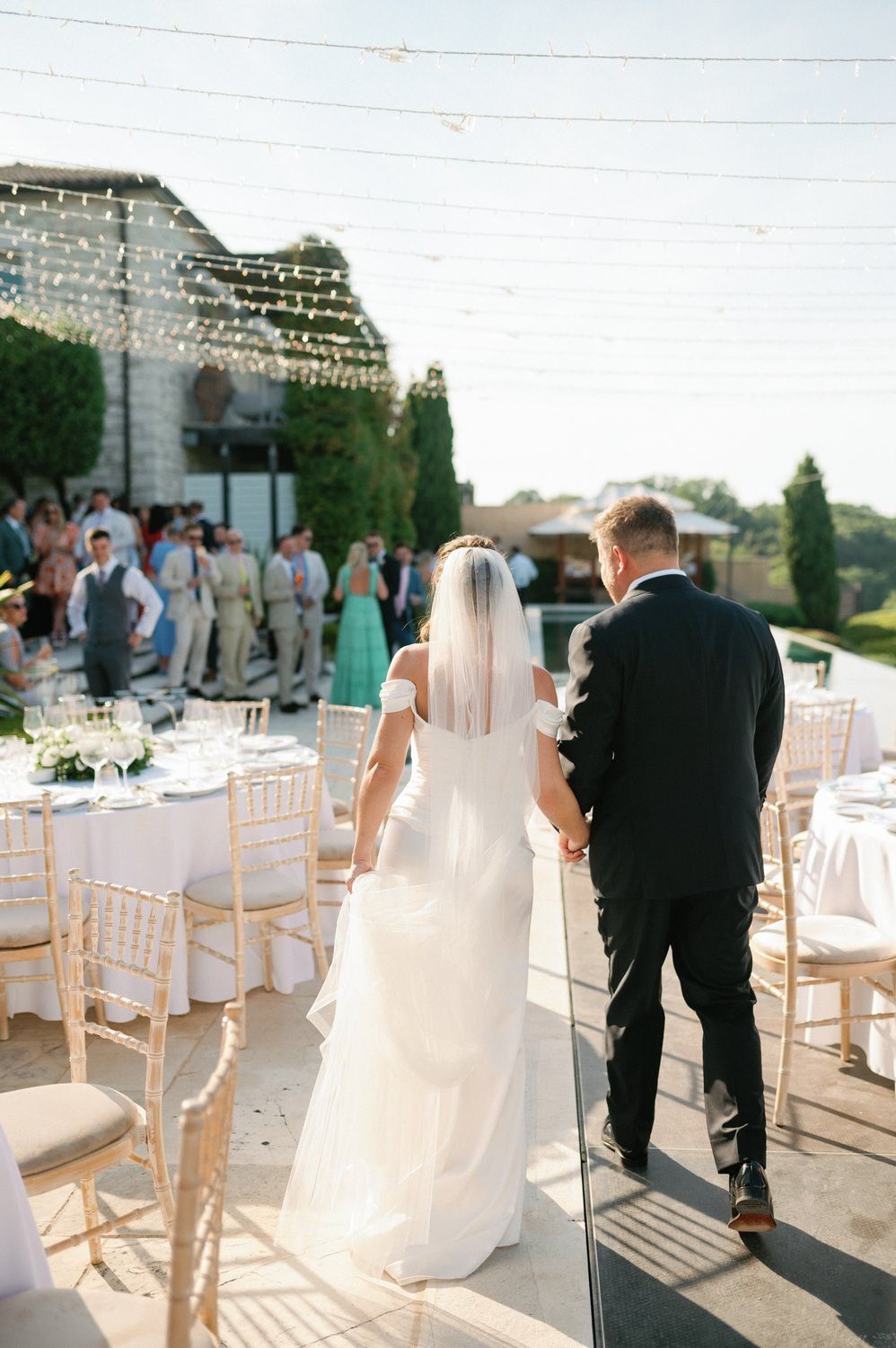Bride and groom walking between elegant outdoor reception tables at sunset.