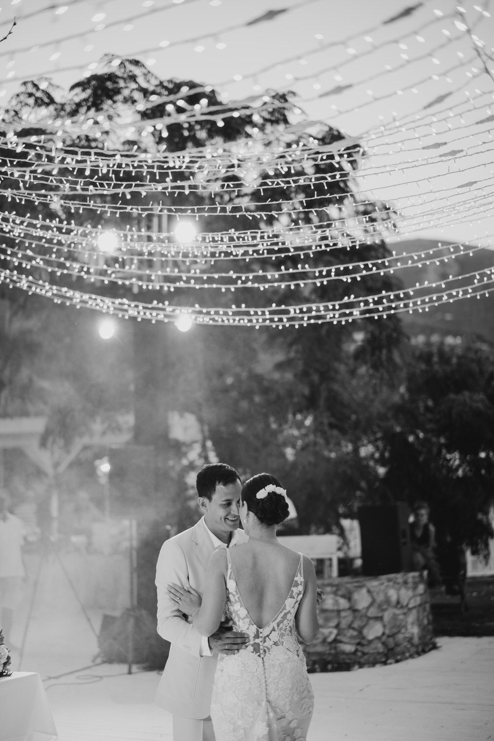 A romantic couple shares their first dance under twinkling string lights at an outdoor wedding reception.