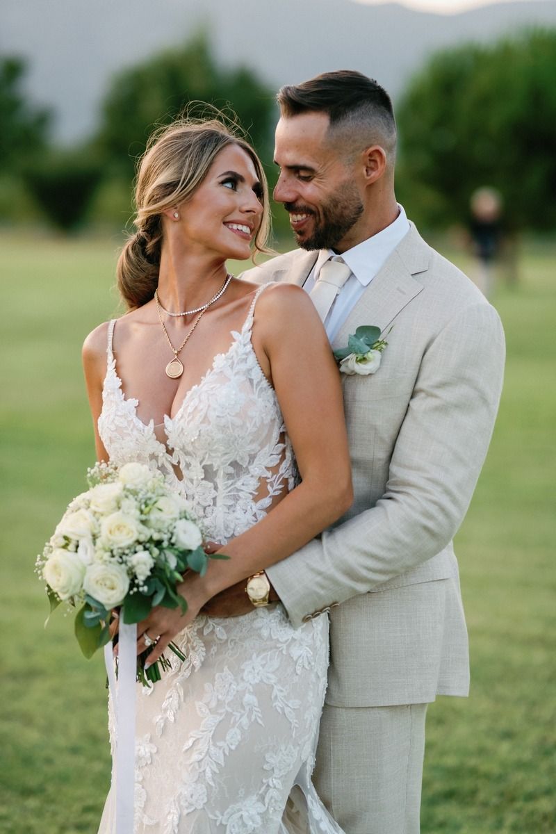 Wedding couple in elegant attire sharing romantic moment in outdoor garden setting.