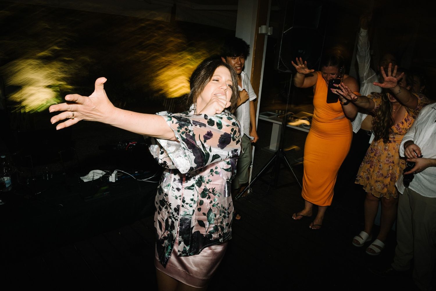 Guests dancing energetically at a wedding reception with festive party outfits and dynamic movement captured on camera.